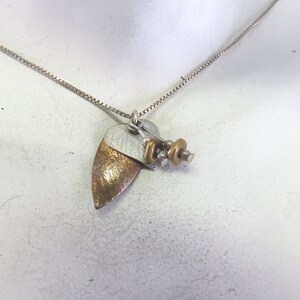 May include: A silver chain necklace with a pendant featuring two layered heart-shaped charms, one silver and one gold, with a cluster of small gold beads and metal accents.