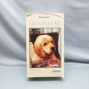 May include: Latch hook kit for a golden retriever puppy pillow. The kit includes yarn and instructions to create a 12x12 inch pillow. The image shows the finished product, a cute puppy with the words "Just Labs" on the pillow.