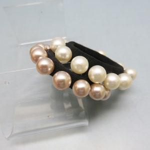 May include: A black hair tie with two rows of pearls. The pearls are a mix of white and light brown.