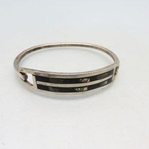 May include: Silver bangle bracelet with a rectangular black inlay featuring two horizontal silver stripes. The black inlay is accented with iridescent abalone shell pieces. The bracelet has a simple, elegant design.