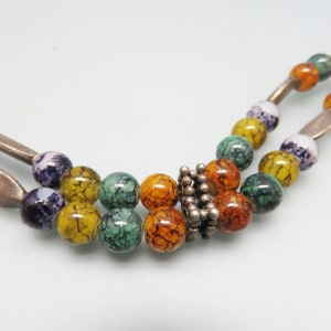 May include: A multi-strand necklace with colorful, marbled beads and a silver clasp. The beads are in shades of green, yellow, orange, and purple.