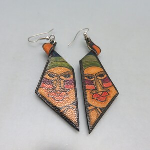 May include: A pair of leather earrings with a geometric diamond shape. Each earring features a painted face with green, orange, red, and black details.