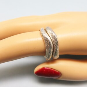 May include: Two silver rings with a textured finish, worn on a model's finger.