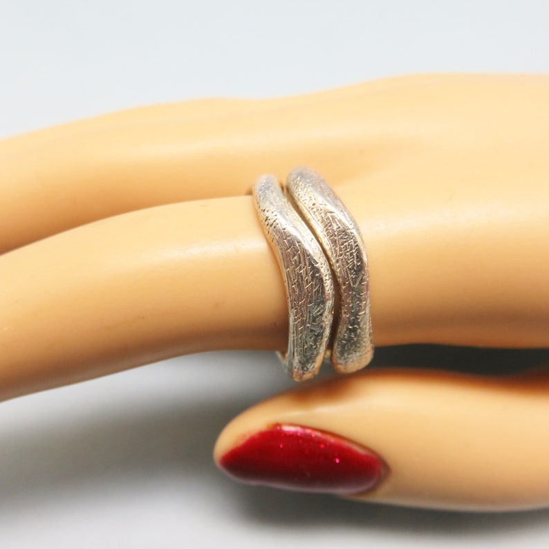May include: Two silver rings with a textured finish, worn on a model's finger.