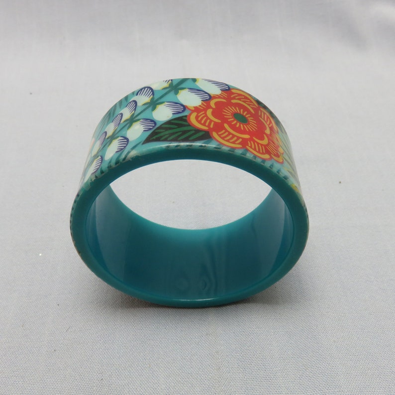 Op de afbeelding: Een turquoise bangle armband met een bloemenpatroon. De bloemen zijn rood, oranje, geel en wit.