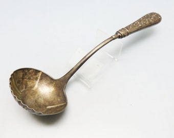 May include: A silver ladle with an ornate handle. The handle is decorated with a floral design. The ladle is in good condition, with some signs of wear.