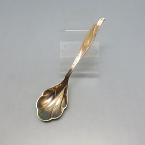 May include: A silver sugar spoon with a decorative, scalloped bowl and a floral design on the handle.