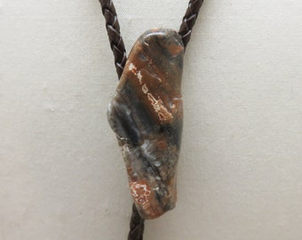 May include: A brown leather bolo tie with a large, irregularly shaped, brown, white, and orange stone pendant.