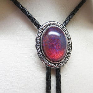 May include: A silver bolo tie with a red and purple iridescent oval stone set in a decorative silver frame. The tie is made of black braided leather.