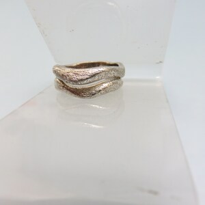 May include: A silver ring with a textured, wavy design. The ring is made of two bands that are intertwined.