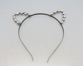May include: A silver-toned headband with cat ears. Each ear is outlined with iridescent, teardrop-shaped rhinestones. The headband is thin and simple, with the ends slightly curved.