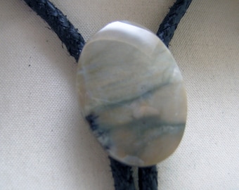 May include: A bolo tie with a light gray oval stone featuring brown and black streaks. The bolo tie has a black leather cord.