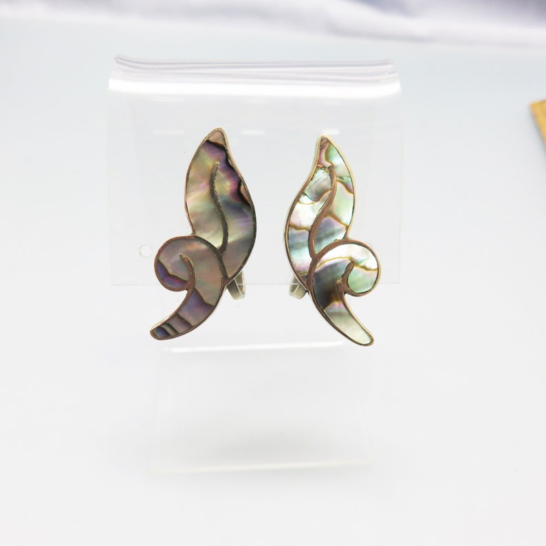 May include: A pair of silver clip-on earrings with a swirl design made from iridescent abalone shell.
