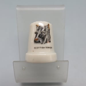 May include: White ceramic thimble with a black and brown illustration of a Scottish Terrier dog's head. The text "SCOTTISH TERRIER" is printed below the image.