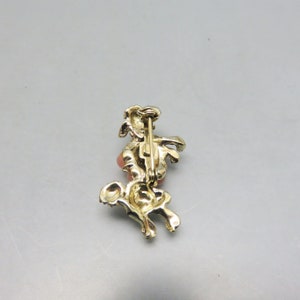 May include: Gold tone brooch featuring a stylized horse with a pink rhinestone. The brooch has a pin back closure.