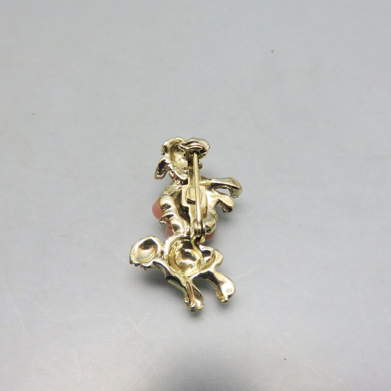 May include: Gold tone brooch featuring a stylized horse with a pink rhinestone. The brooch has a pin back closure.
