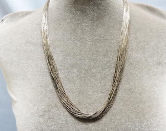 May include: A silver chain necklace with multiple strands, creating a layered effect. The necklace is displayed on a mannequin.
