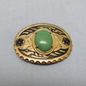 May include: A gold-tone belt buckle with a green stone inlay and black floral designs.