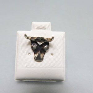 May include: A silver bull head charm with a textured surface. The charm is displayed on a white background.