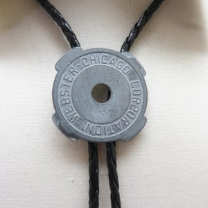 May include: A black leather bolo tie with a silver metal bolo slide that says "Webster-Chicago Corporation".