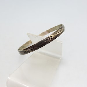 May include: A silver bangle bracelet with a delicate leaf pattern etched into the surface.