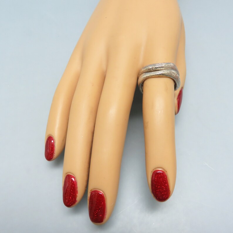 May include: A silver double band ring on a model's finger with red nail polish.