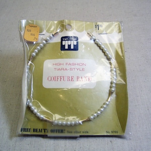 May include: A white pearl and gold tiara-style hair band on a yellow and white packaging card. The card reads "Tip-Top High Fashion Tiara-Style Coiffure Band" and "Free Beauty Offer! See other side. No. 9765".