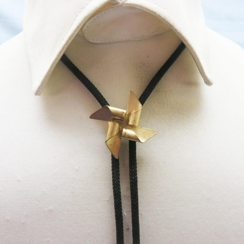 May include: A black bolo tie with a gold pin shaped like a pinwheel.