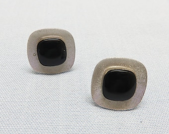 May include: A pair of silver cufflinks with black square-shaped stones in the center.