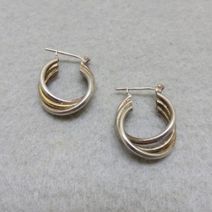 May include: A pair of silver hoop earrings with a twisted design. The earrings are made of two different metals, one silver and one gold.