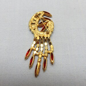 Pode incluir: Um broche dourado com um design de strass vermelho. O broche tem a forma de uma l&aacute;grima com uma franja de strass vermelhos pendurados.