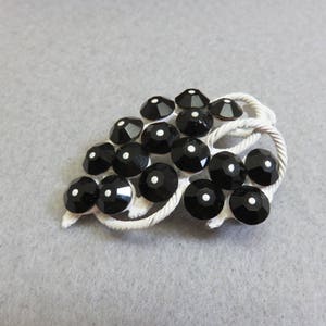 May include: A white metal brooch shaped like a bunch of grapes with black rhinestones.