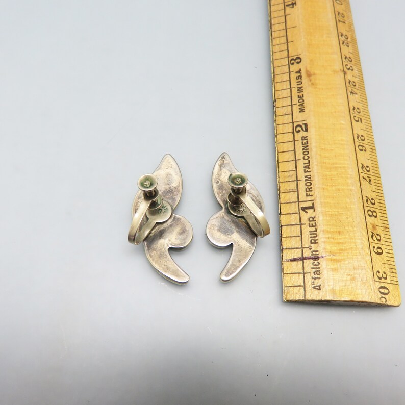 May include: A pair of silver tone clip-on earrings with a swirl design. The earrings are about 1 inch long.