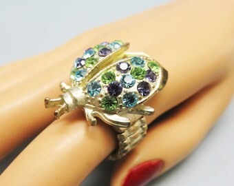 May include: A gold-toned ring with a multi-colored jeweled beetle design. The ring is adjustable and has a band made of linked metal pieces.
