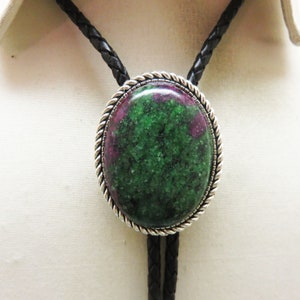 May include: A green and pink gemstone bolo tie with a silver-toned setting. The bolo tie has a braided black leather cord.