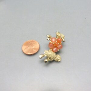 May include: A gold-toned brooch in the shape of a poodle with a cluster of pink and orange rhinestones on its back.