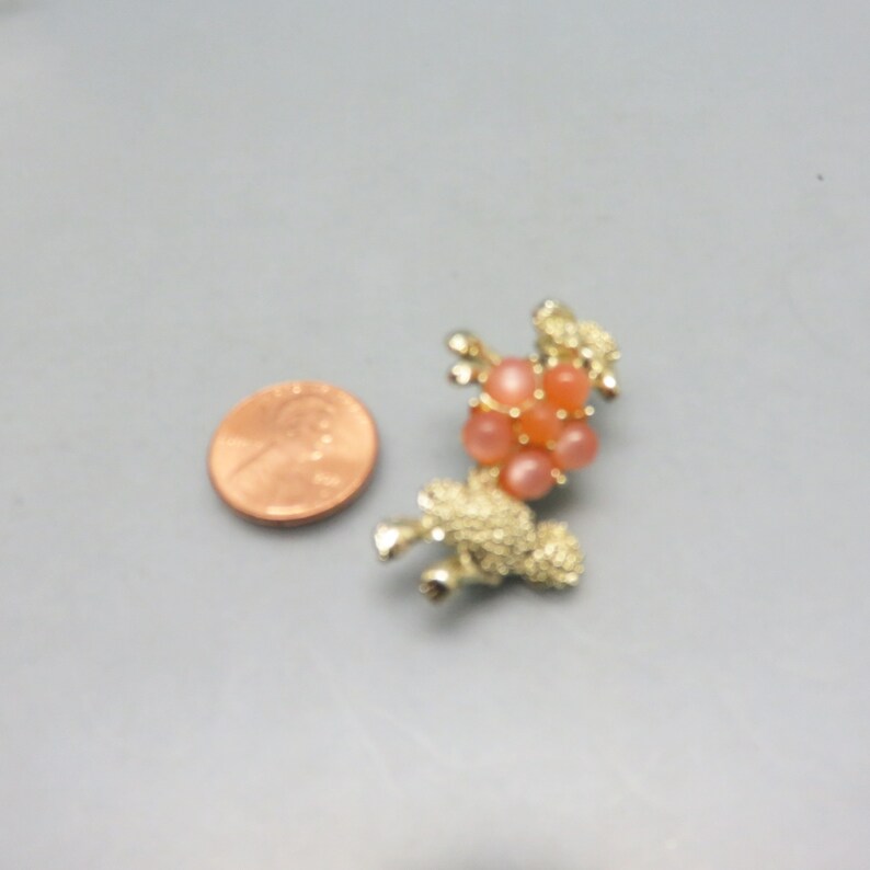 May include: A gold-toned brooch in the shape of a poodle with a cluster of pink and orange rhinestones on its back.