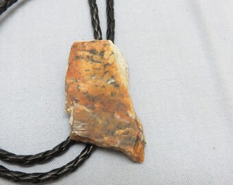 May include: A bolo tie with a brown leather cord and a large, irregularly shaped, orange and brown stone pendant.