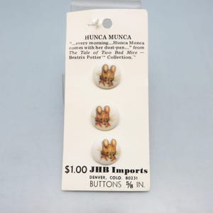 May include: A card of three round buttons featuring the character Hunca Munca from Beatrix Potter's "The Tale of Two Bad Mice." Each button has a detailed illustration of the character. The card also includes text about the character and the button size.