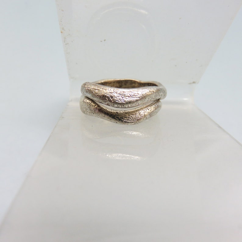 May include: A silver ring with a textured, wavy design. The ring is made of two bands that are intertwined.
