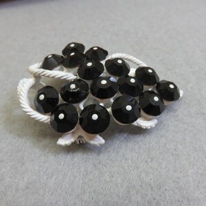 May include: A white metal brooch with a grape cluster design. The grapes are made of black glass with white centers.
