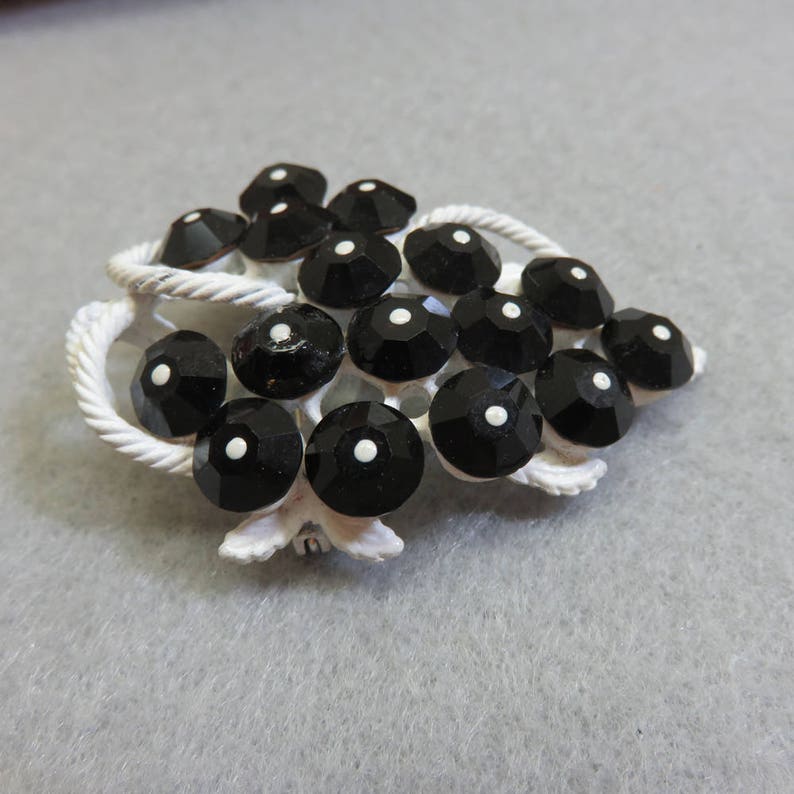 May include: A white metal brooch with a grape cluster design. The grapes are made of black glass with white centers.