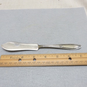 May include: A silver butter knife with a decorative handle and a pointed blade. The knife is 7 inches long.