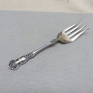 以下が含まれることがあります： 花柄の装飾が施されたハンドルを持つ銀製のフォーク。フォークは3本の歯があり、状態は良好です。
