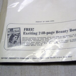 May include: A vintage advertisement for a 240-page beauty book. The ad features a woman with long, dark hair and a white dress. The text reads "FREE! Exciting 240-page Beauty Book".