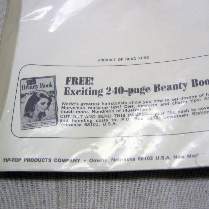 May include: A vintage advertisement for a 240-page beauty book. The ad features a woman with long, dark hair and a white dress. The text reads "FREE! Exciting 240-page Beauty Book".