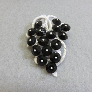 May include: A white metal brooch shaped like a bunch of grapes with black rhinestones. The rhinestones have a white dot in the center.