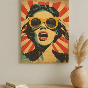 May include: Pop art style canvas print featuring a woman with yellow sunglasses and an open mouth. The background has a red and yellow sunburst design. The artwork is mounted on a wooden frame, adding a vintage aesthetic to the piece.