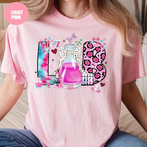 May include: Light pink t-shirt with a colorful "LAB" graphic. The design includes a beaker with a bow, a microscope, test tubes, and the letter "B" in a pink leopard print. The word "LIGHT PINK" is in a pink circle in the upper left.