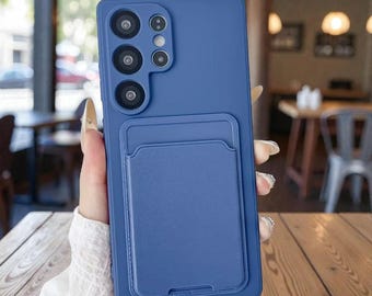 Puede incluir: Funda de teléfono azul con un tarjetero integrado. La funda tiene un acabado mate y presenta un módulo de cámara con múltiples lentes. El tarjetero es azul a juego y está adherido a la parte posterior de la funda.